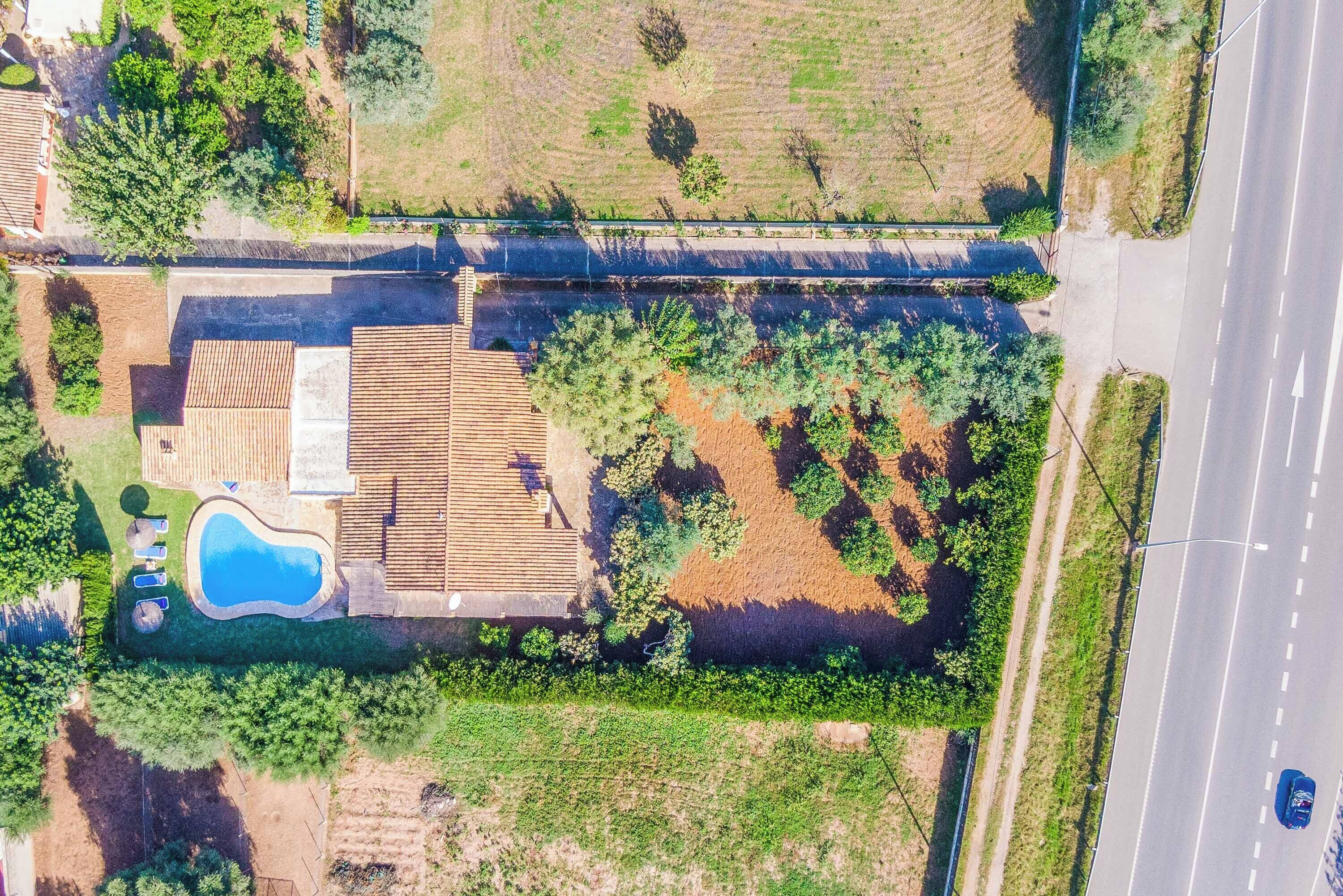 Ovenudblik over et boligområde med swimmingpool, træterrasse og en vej ved siden af et marker.