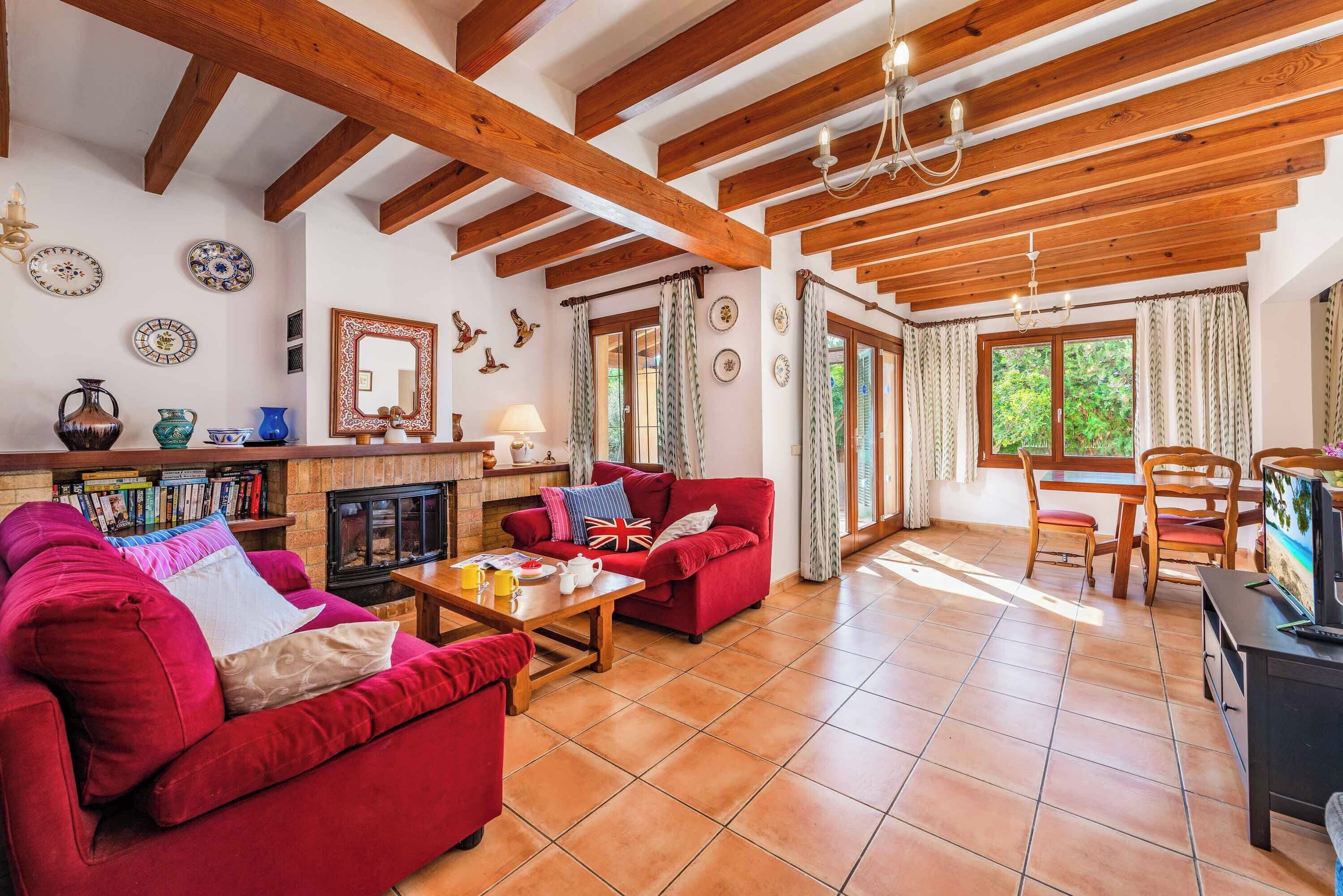 A spacious living room with a fireplace, red sofas, wooden beams, and a dining area with chairs.