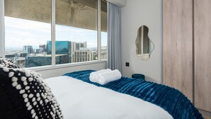 Ein Hotelzimmer mit großem Fenster, einem Bett mit blauer und weißer Bettdecke, einem Holzschrank und einem runden Spiegel an der Wand.
