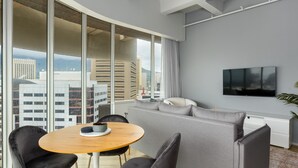 Ein modernes Wohnzimmer mit einer Couch, Sesseln, einem Fernseher und Blick auf Gebäude.