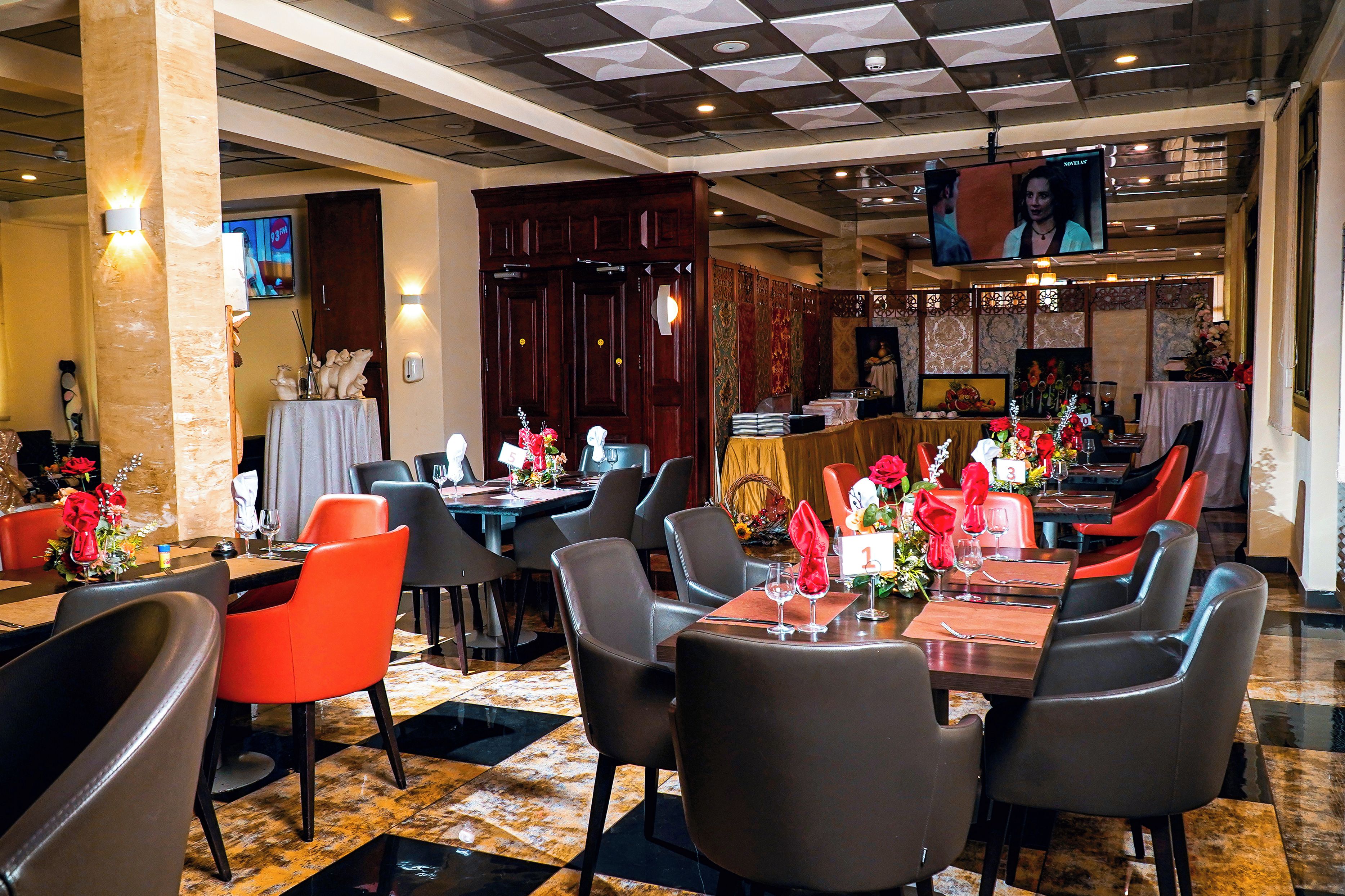 Un comedor de hotel con varias mesas, sillas y una pantalla de televisión.