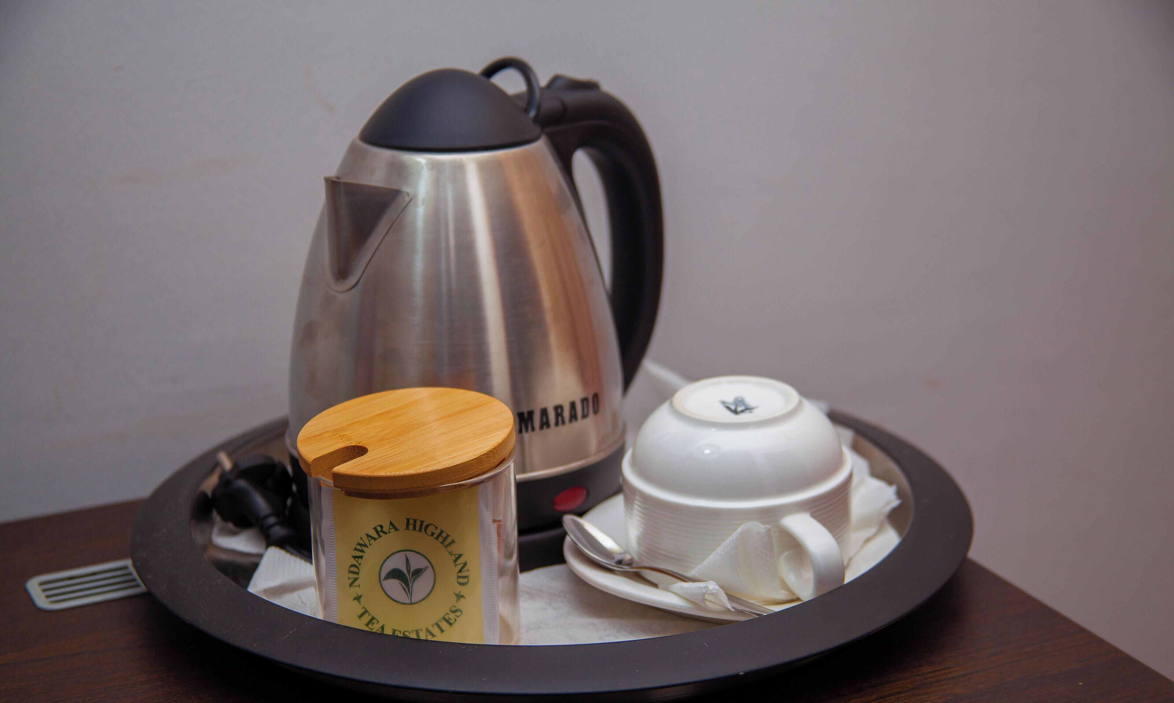 A tray with a stainless steel coffee pot, a wooden container with a lid, and a white teacup with saucer.