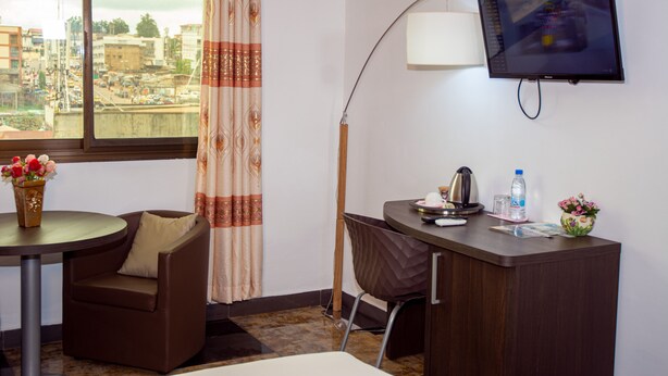 A hotel room with a desk, chair, and a TV mounted on the wall. - New Heaven Hôtel (Yaoundé)
