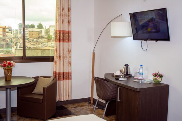 A hotel room with a desk, chair, and a TV mounted on the wall. - New Heaven Hôtel (Yaoundé)