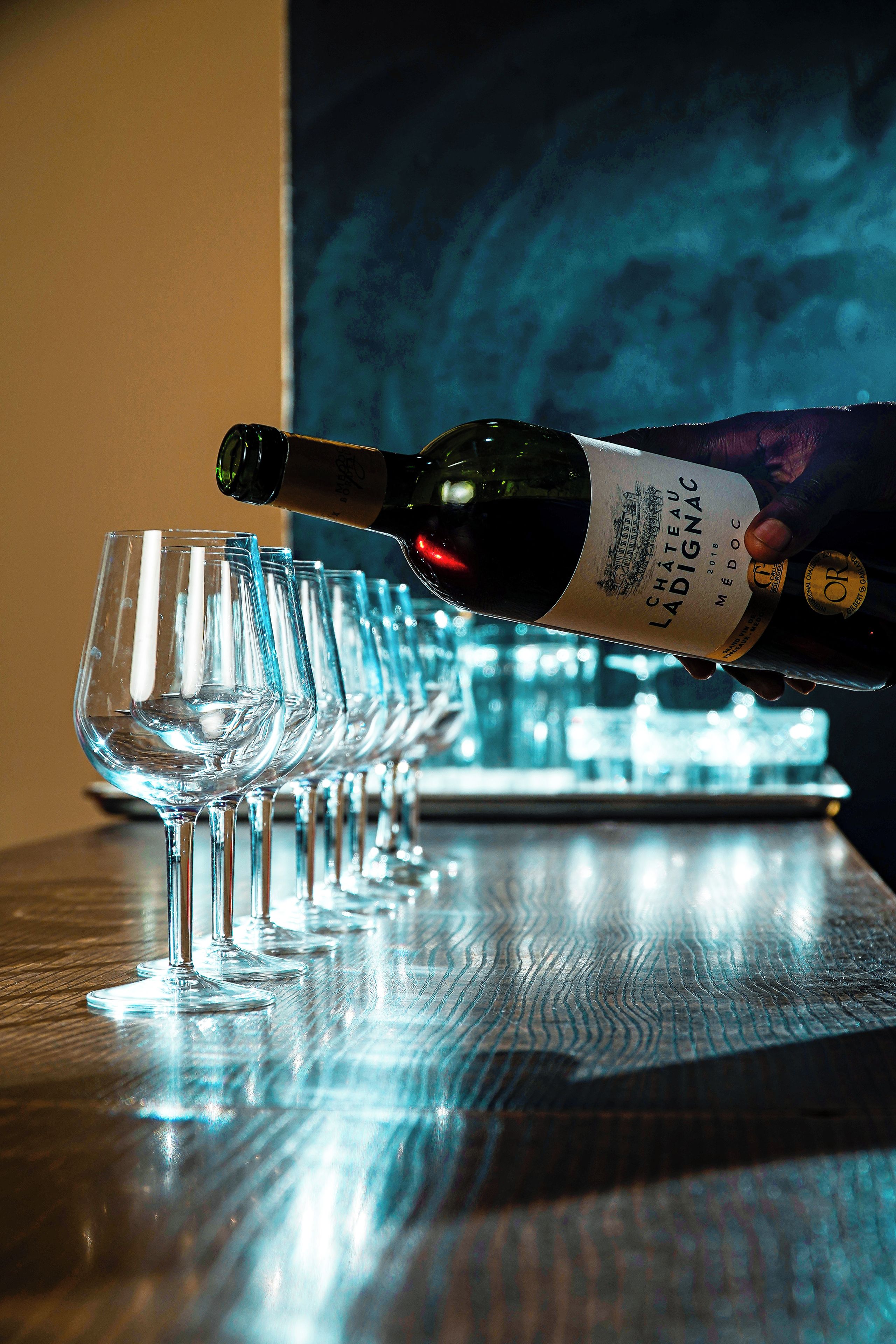 Una botella de vino siendo servida en una fila de copas sobre una mesa de madera.