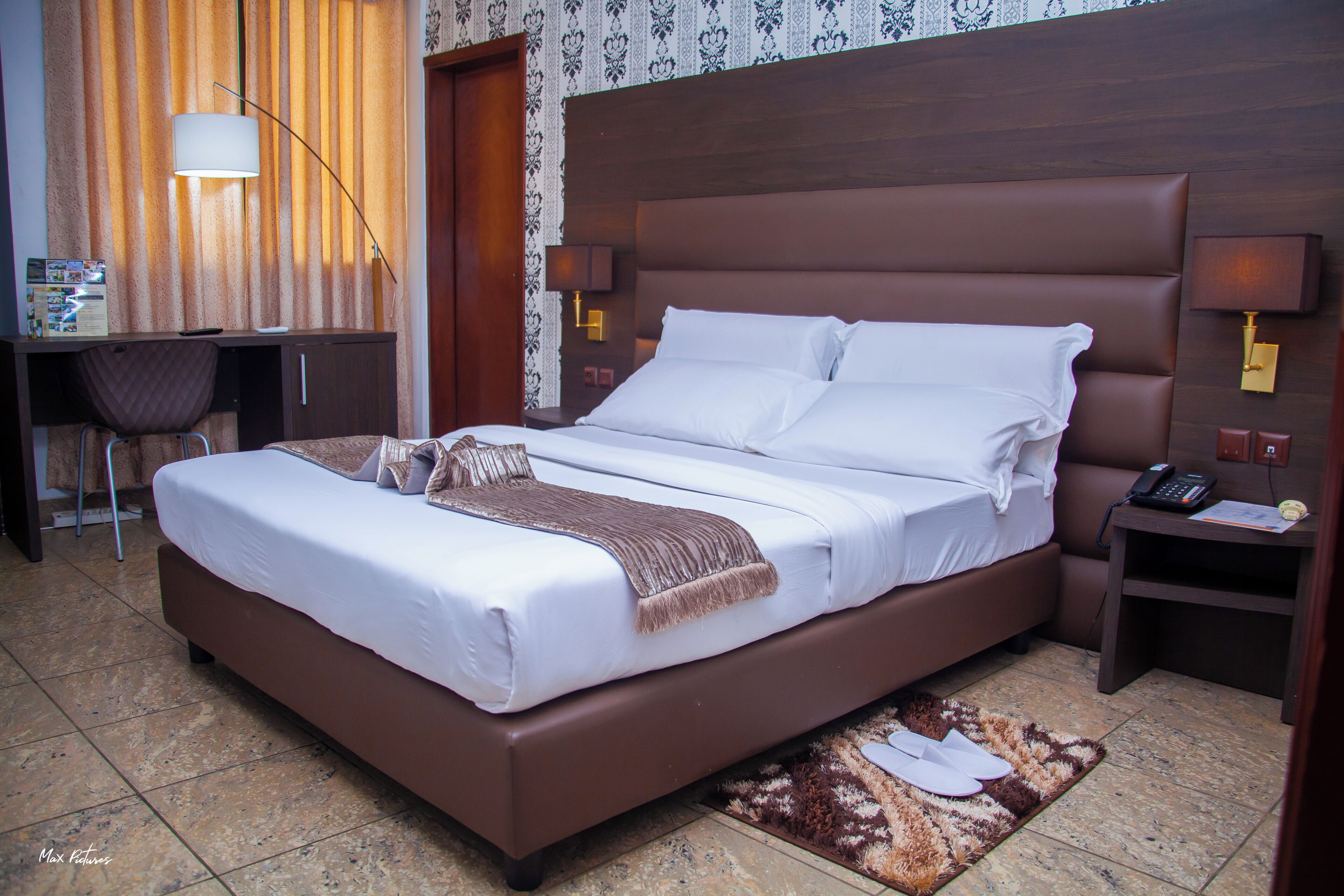 A hotel room with a large bed, a desk with a chair, a lamp, and a telephone.