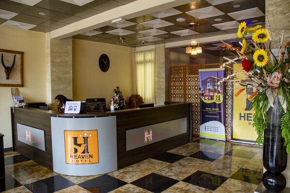 A reception desk with a checkered floor, a clock, and a decorative vase with flowers. - New Heaven Hôtel (Yaoundé)