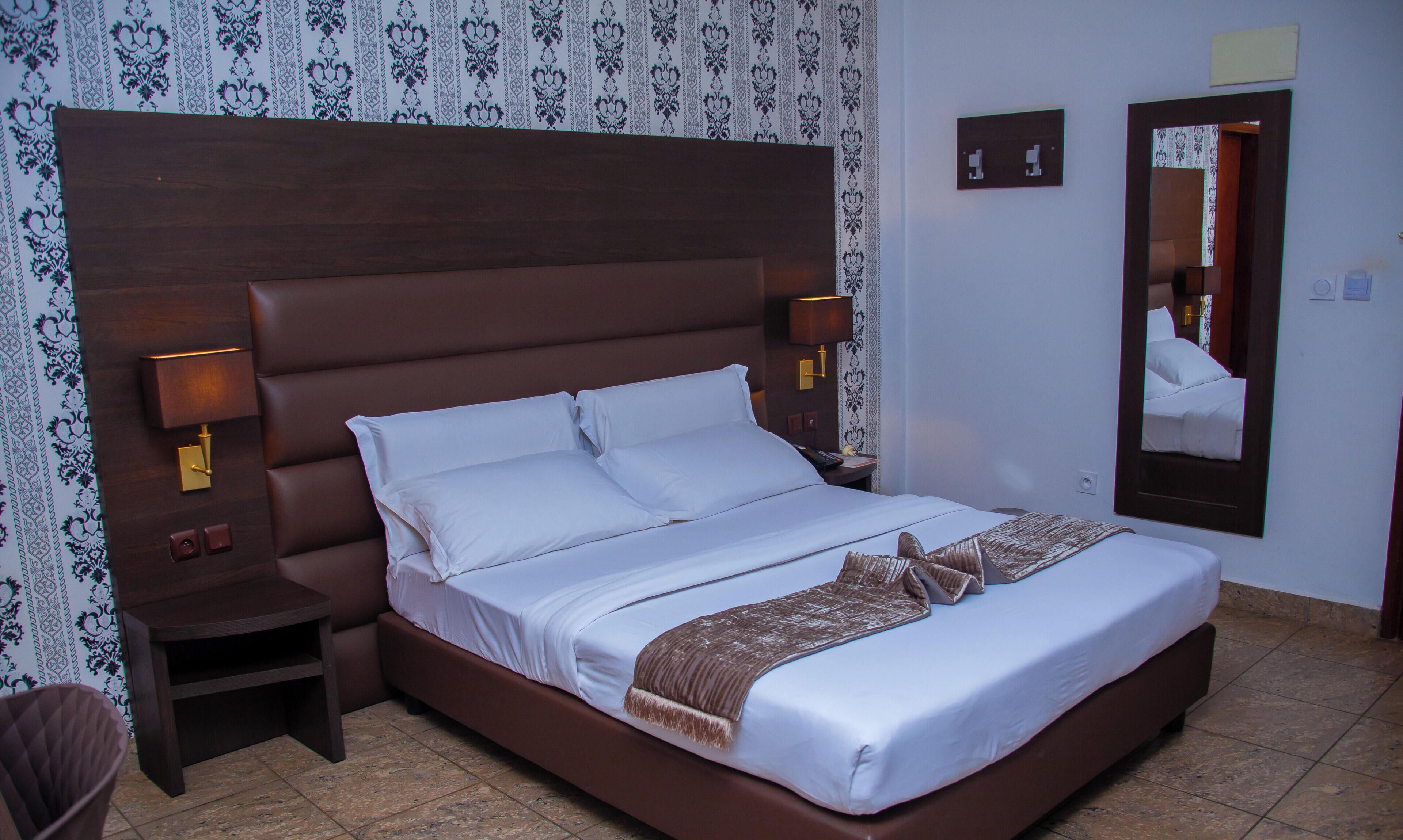 A hotel room with a large bed, a nightstand, a mirror, and patterned wallpaper.
