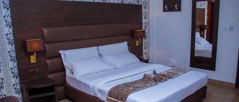 A hotel room with a large bed, a nightstand, a mirror, and patterned wallpaper.