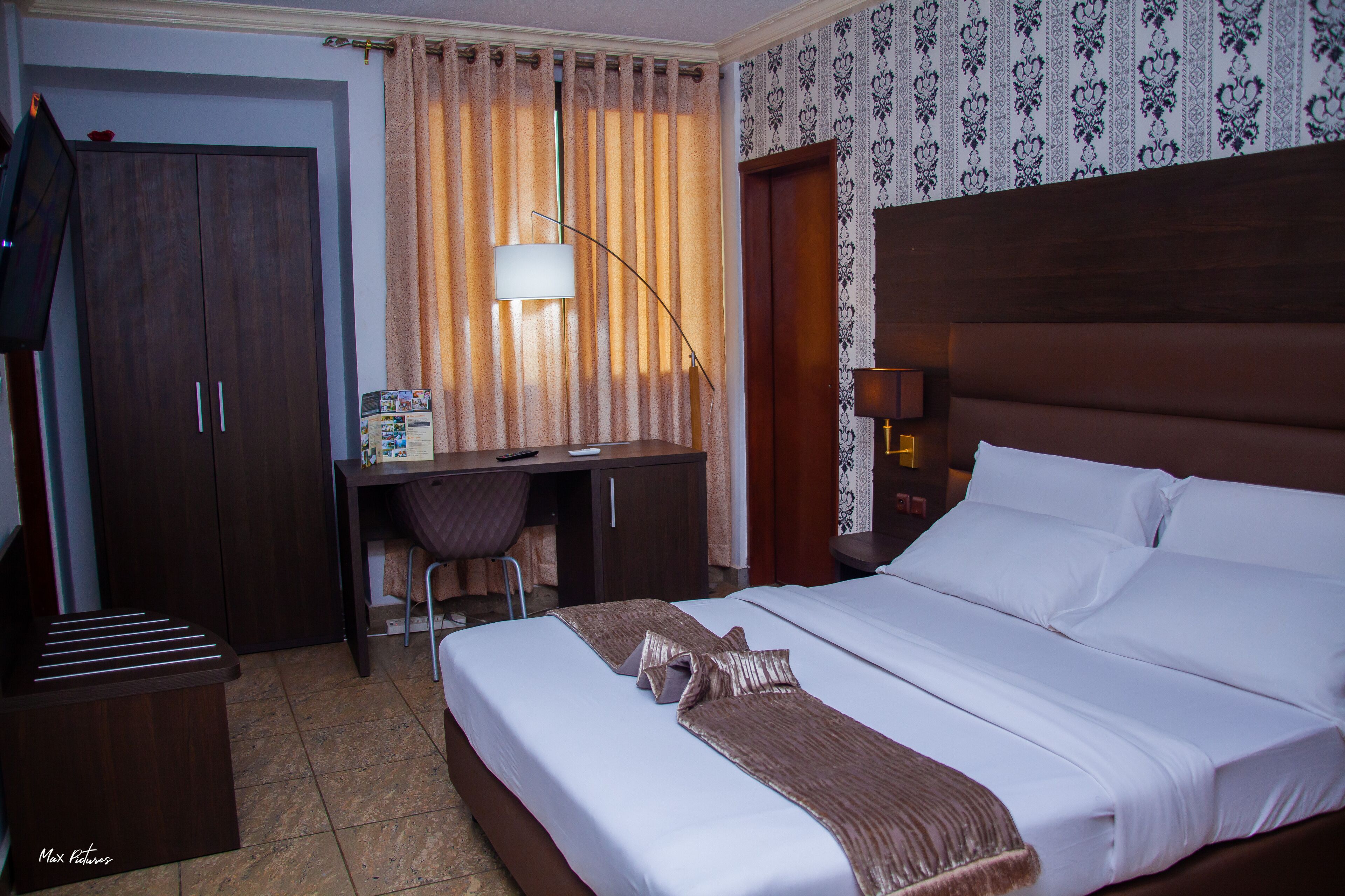 A hotel room with a bed, a desk, a chair, a wardrobe, and a television.