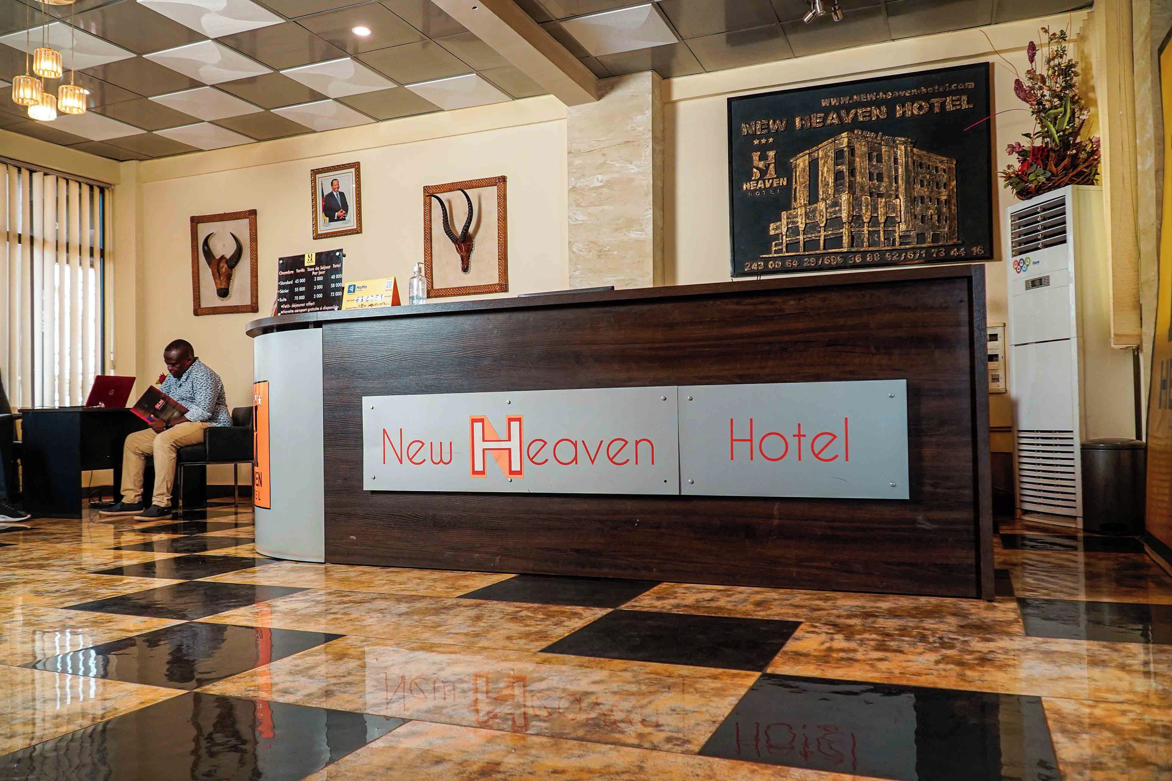 A reception desk with 'New Heaven Hotel' signage, a check-in counter, a framed bull's head decoration, and a poster of the hotel building.