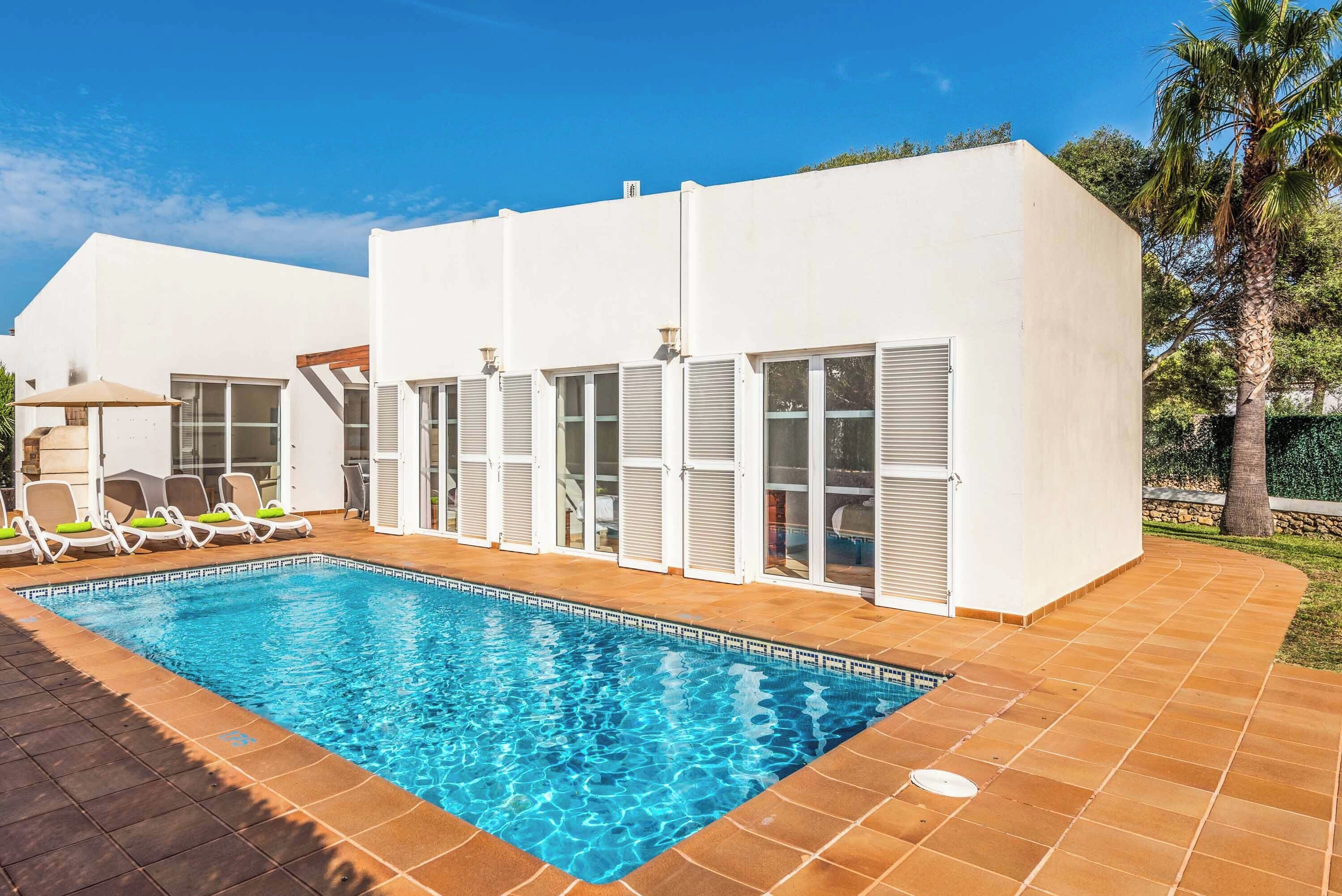 A modern poolside area with a clear blue pool, white walls, and a tiled deck.