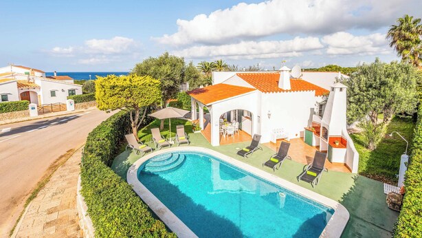 A modern villa with a swimming pool, outdoor seating, and a view of the sea.