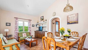A cozy living room with a sofa, a dining table set for four, and a kitchen area with a TV and cabinets.