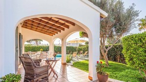 A covered outdoor seating area with wicker furniture, a pool, and a well-maintained garden.