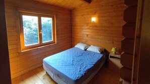 Ein Zimmer in einer Holzhütte mit einem Bett, einem Fenster und einem Nachttisch.
