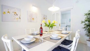 A dining area with a white table, blue cushioned chairs, a vase with yellow flowers, and wall art.