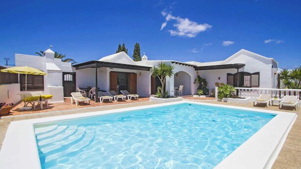 A poolside area with a clear blue pool, white buildings, and sun loungers.