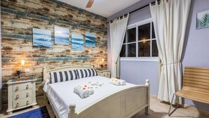 Ein Schlafzimmer mit Holzwand, einem Bett mit weißer Bettwäsche, einem Nachttisch, einer Bank und einem Fenster mit Vorhängen.