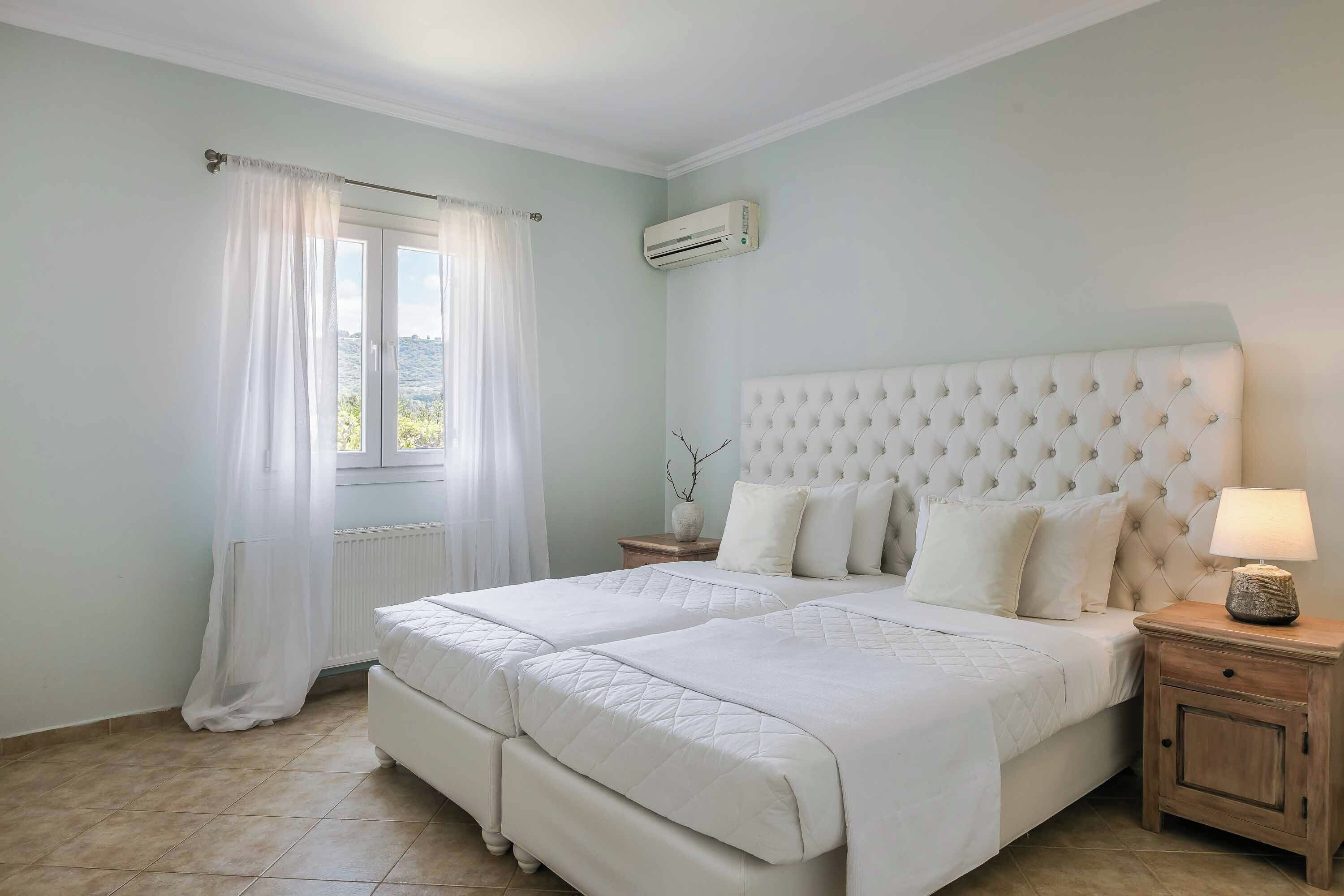 A bedroom with a double bed, a nightstand, a lamp, and an air conditioning unit.