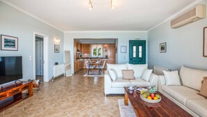 A spacious living room with a television, a wooden coffee table with fruit, a white sofa, and a kitchen in the background. - Villa Tramonto Minies (Ionian Islands)