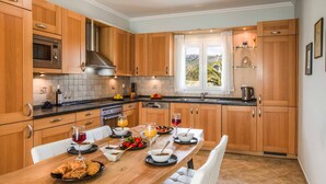 A modern kitchen with wooden cabinets, a built-in oven, and a dining table set with breakfast items. - Villa Tramonto Minies (Ionian Islands)