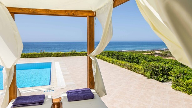A poolside area with a view of the sea, a wooden pergola, and a small table with a towel. - Villa Tramonto Minies (Ionian Islands)