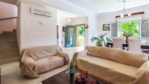 A living room with two beige sofas, a coffee table with a bottle and glass, and a staircase to the left. - Villa Mirela Mikri - Three Bedroom Villa, Sleeps 6 (Corfu)