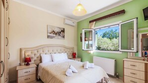 A bedroom with a large bed, bedside tables, a nightstand, a mirror, and a window with an open shutter. - Villa Mirela Mikri - Three Bedroom Villa, Sleeps 6 (Corfu)