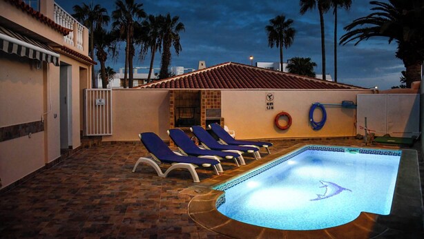 Una piscina con sillas de descanso y palmeras al fondo.