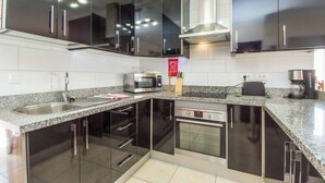 Una cocina moderna con armarios negros, electrodomésticos de acero inoxidable, un lavamanos doble y un horno empotrado.