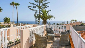 Un balcón con muebles de mimbre, una palmera y vista al mar.