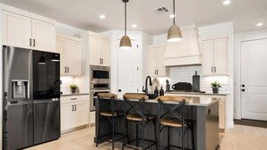 A modern kitchen with stainless steel appliances, white cabinetry, and a central island with bar stools. - The Sanctuary at Desert Color: Lagoon + Beaches (St. George)
