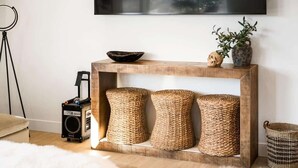 A wooden console table with woven baskets and a bowl on top, a speaker, and a potted plant on a white wall. - The Sanctuary at Desert Color: Lagoon + Beaches (St. George)