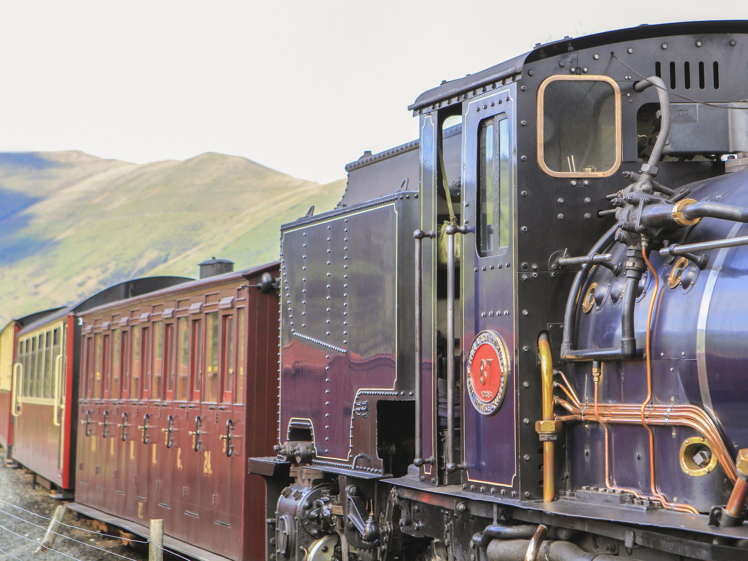 A vintage steam locomotive with a carriage, set against a mountainous backdrop.