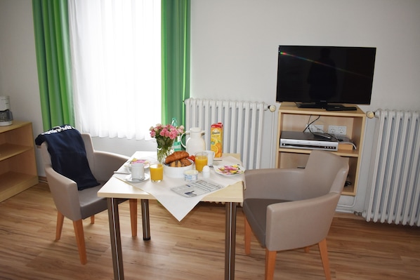 Un comedor con una mesa dispuesta para dos personas, un televisor sobre un mueble bajo y un radiador al fondo.