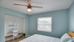 A bedroom with a bed, a ceiling fan, a window with blinds, and a white shelving unit against the wall. - New and cozy 2/1 near River (Micco)
