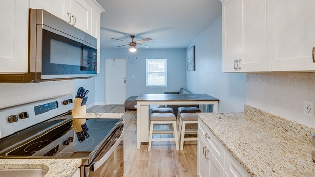 A modern kitchen with white cabinets, a built-in microwave, a stove, and a dining area with stools. - New and cozy 2/1 near River (Micco)