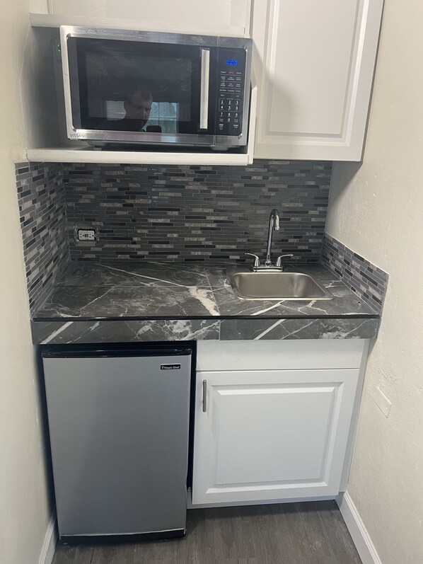 A compact kitchen with a built-in microwave, a sink, and a compact refrigerator.