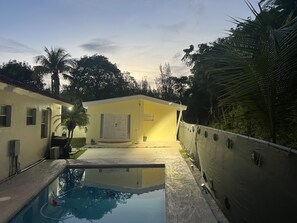 A residential property with a swimming pool, a yellow house, and surrounding greenery.