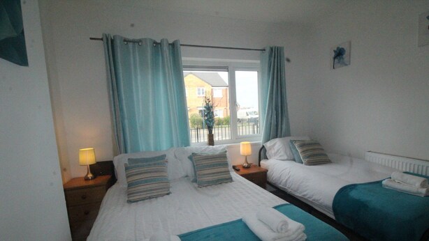 A hotel room with two beds, each with a blue bedspread and white linens, a window with curtains, and a view of a building outside. - Doe Quarry (Sheffield)