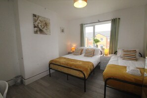 Habitación doble con dos camas, una ventana con cortinas, una mesita de noche con lámpara y un cuadro en la pared.