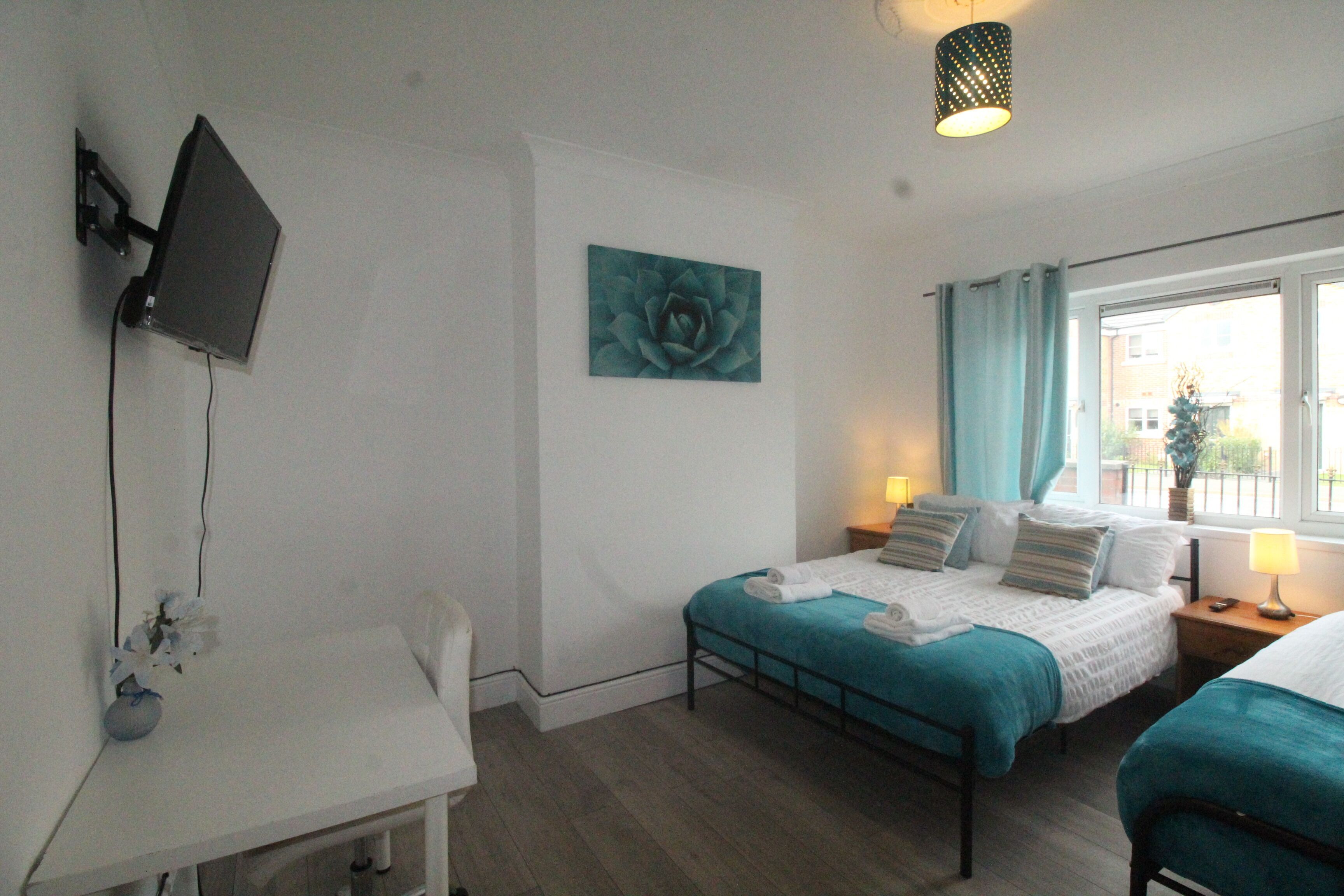 Een slaapkamer met een bed, een bureau, een aan de muur bevestigde televisie en een raam met gordijnen.