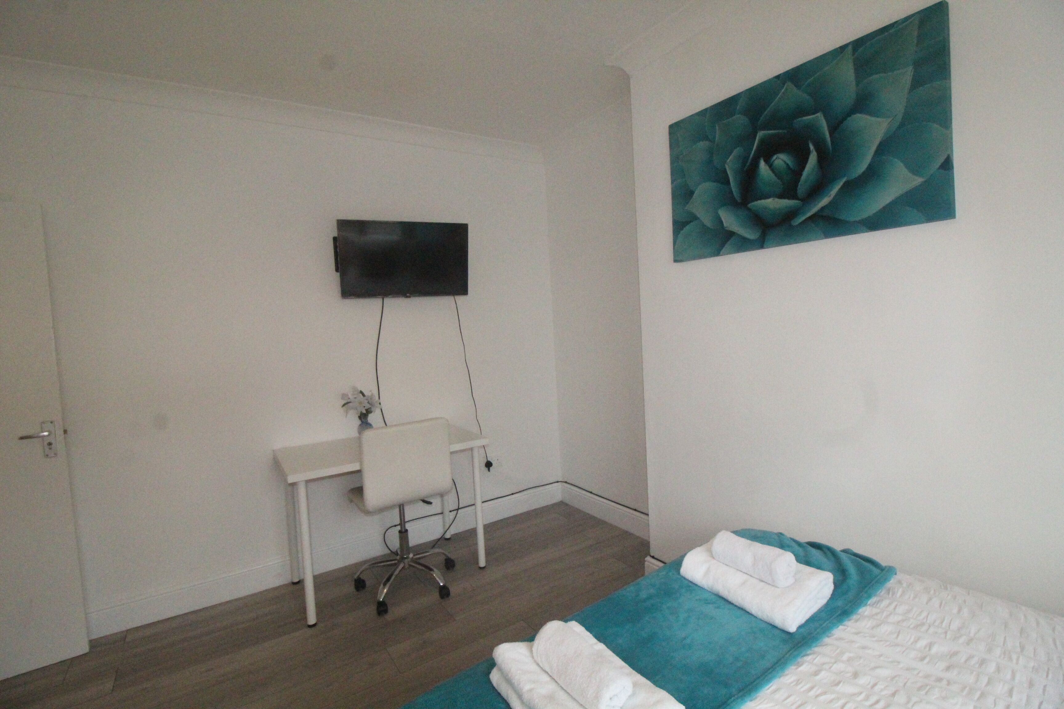 A bedroom with a bed, a desk, and a TV mounted on the wall.
