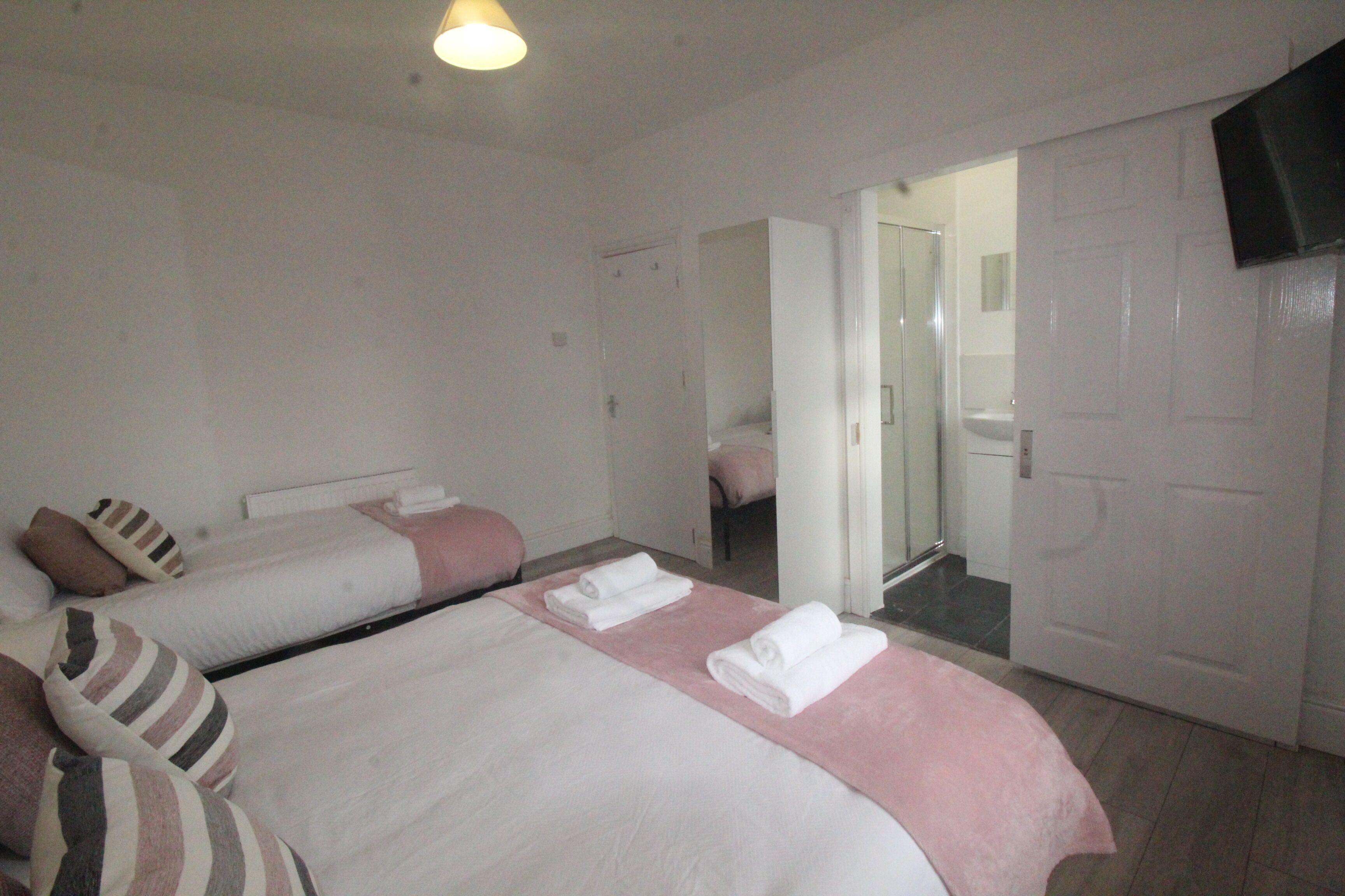 A hotel room with two beds, a shower area, and a television mounted on the wall.