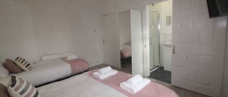 A hotel room with two beds, a shower area, and a television mounted on the wall.