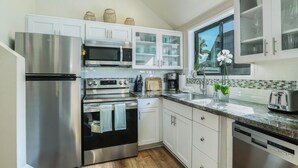 A modern kitchen with stainless steel appliances, white cabinetry, and a window with a view of palm trees.
