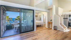 A modern interior with a balcony overlooking the ocean, a spacious bedroom with a large bed, and a kitchen area.
