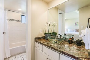 Un baño moderno con un lavamanos de cristal, una ducha y un espejo grande.