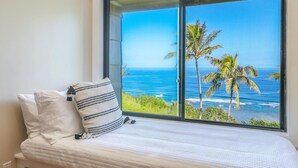 A bedroom with a large window overlooking the ocean and palm trees.
